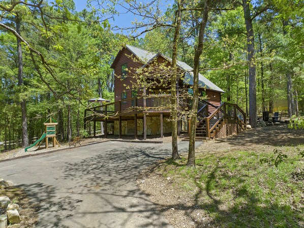 Eine Holzhütte mit einer Terrasse und einer Spielanlage in einem Waldgebiet.
