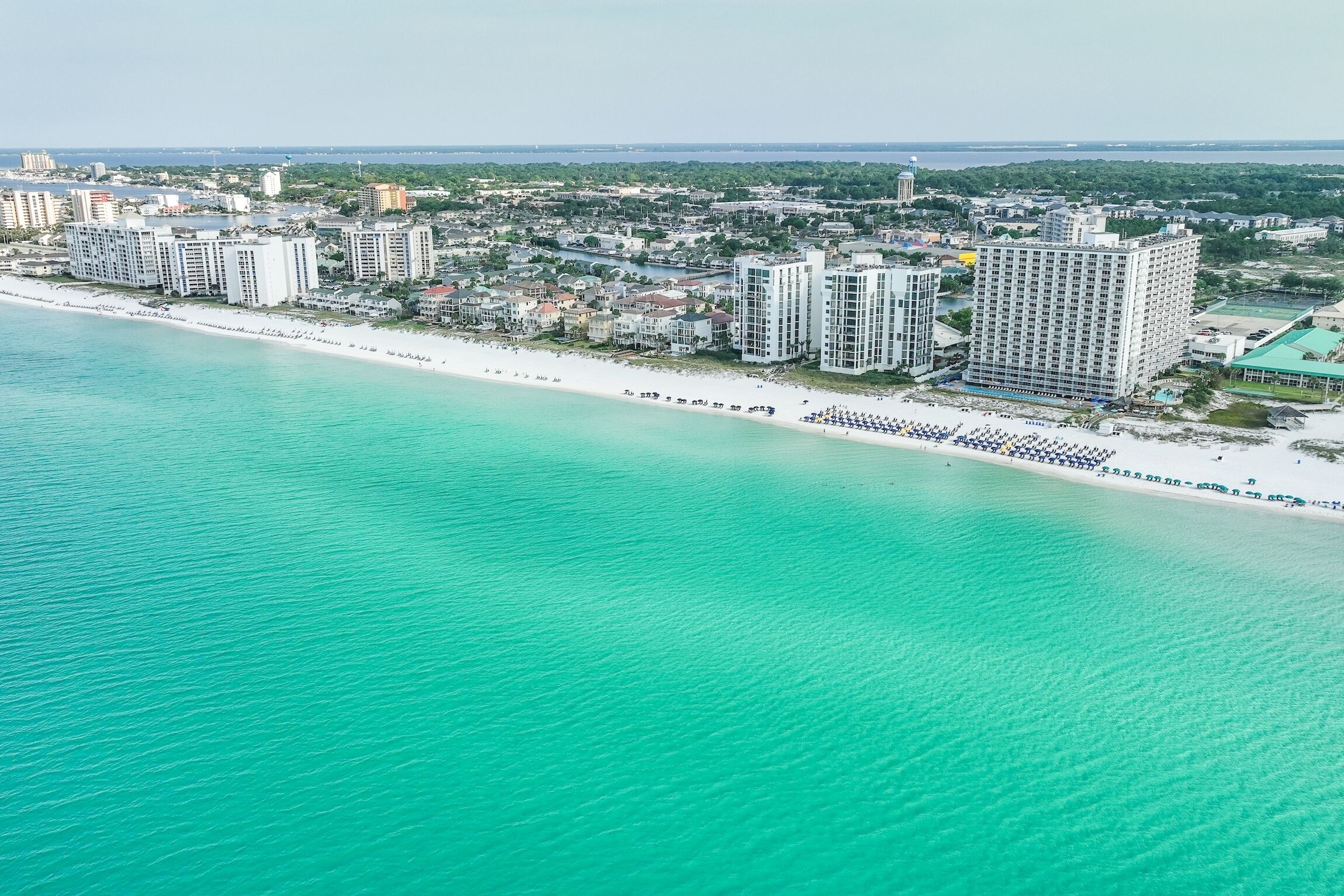 An aerial view of a coastal area with a beachfront hotel, including high-rise buildings and a sandy beach.