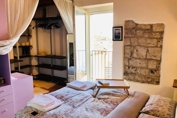 A bedroom with a bed, a bedside table, a wardrobe, and a balcony.