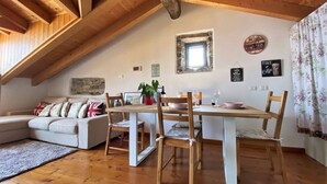 Una accogliente stanza mansardata con zona pranzo, divano e una piccola finestra che dà sulla cucina.