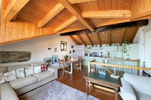 Een gezellige woonkamer met een houten plafond, een stenen muur, een eethoek met een tafel en stoelen, en een keuken met lichte kastjes.