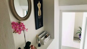 A hallway with a mirror, a framed artwork, pink orchids, a small plant, and a decorative box with a mouse figurine. - Cà Milla Argegno apartment (Argegno)