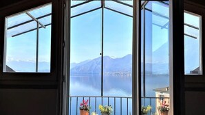 Una stanza con un'ampia porta a vetri che dà su un balcone con vista su un lago e montagne.