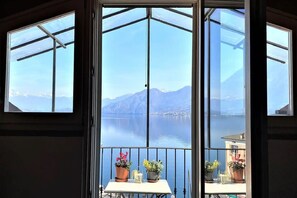 Ein Zimmer mit einer großen Glasdoor, die auf einen Balkon mit Blick auf einen See und Berge führt.