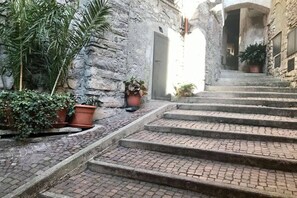 Una estrecha escalera de piedra que conduce a una entrada, rodeada de plantas en macetas y un rústico muro de piedra.