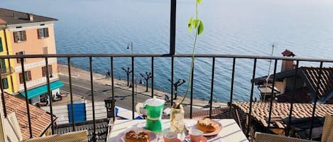 Ein Balkon mit Tisch für zwei Personen, Blick auf ein Wasserufer mit Gebäuden und einem klaren Himmel.