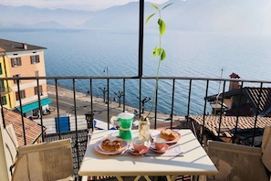 Un balcón con una mesa lista para dos personas, con vista a un frente marítimo con edificios y un cielo despejado.