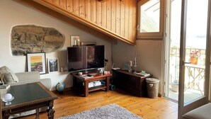 Un accogliente soggiorno con soffitto in legno, parete in pietra, una televisione a schermo piatto, un divano, un tavolino da caffè e un balcone con ringhiera.