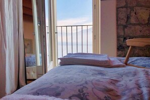 Een slaapkamer met een bed, een balkon met hekwerk en uitzicht op zee.