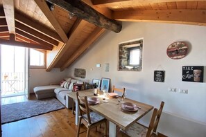 Un comedor acogedor con una mesa de madera dispuesta para dos, una pared de piedra con un reloj y un ventanal pequeño.
