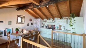 Una cucina rustica con travi in legno, un'area pranzo con sedie e una scala che conduce a un piano superiore.