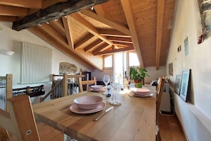 Comedor con una mesa de madera dispuesta para cuatro, una pared de piedra y una escalera que sube a un nivel superior.
