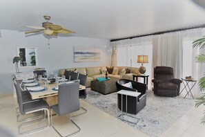 Uma sala de estar moderna com área de jantar, um ventilador de teto, um sofá, uma mesa de centro, uma cadeira e um abajur.