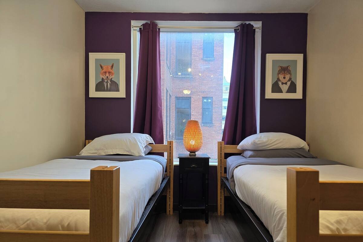 A room with two beds, a nightstand with a lamp, and two framed pictures on the wall.