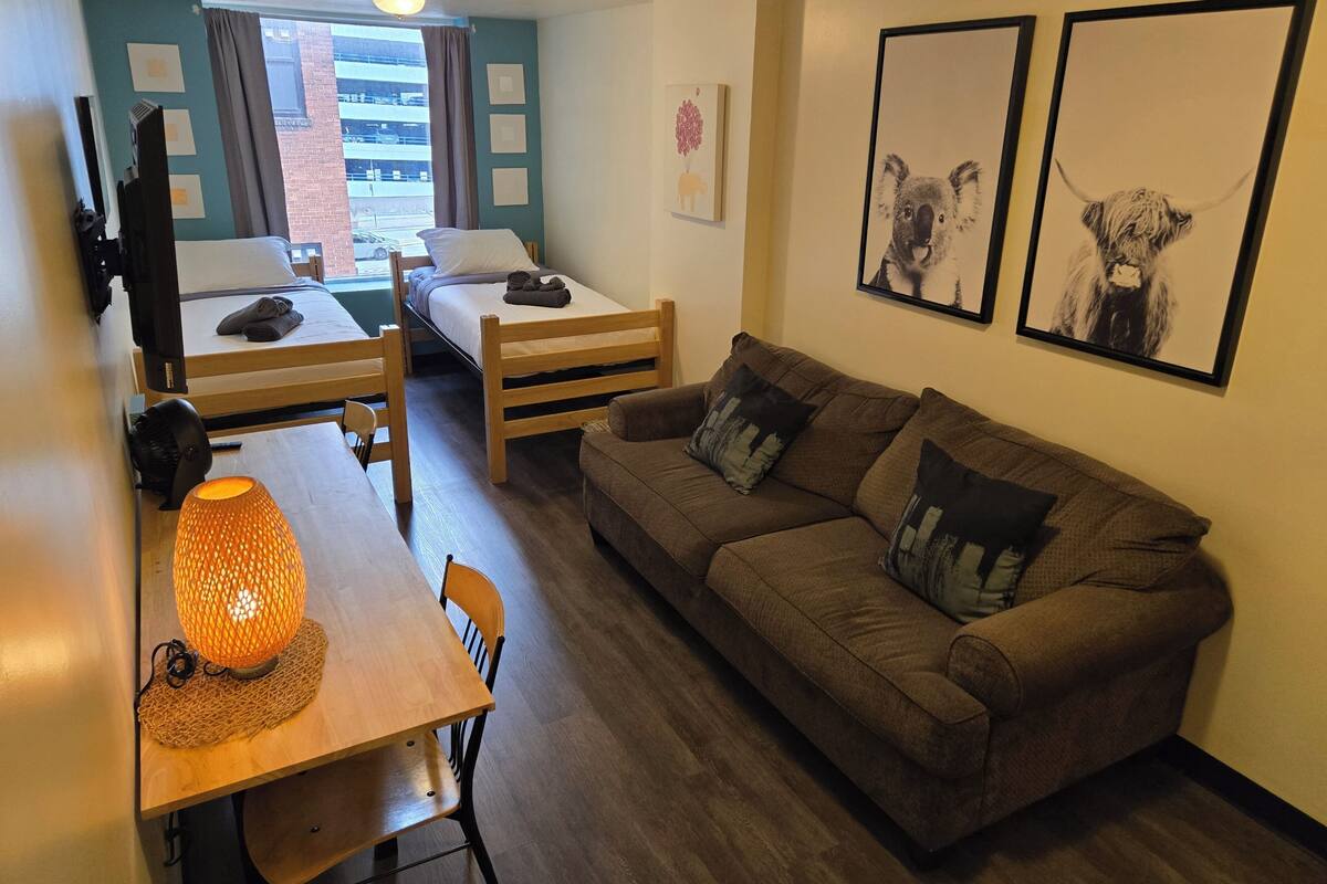 A compact living space with a bunk bed, a sofa, a dining table with a lamp, and artwork on the walls.