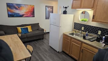 Cocina compacta con refrigerador, armarios de madera, un lavamanos y una zona de comedor con mesa y sillas.