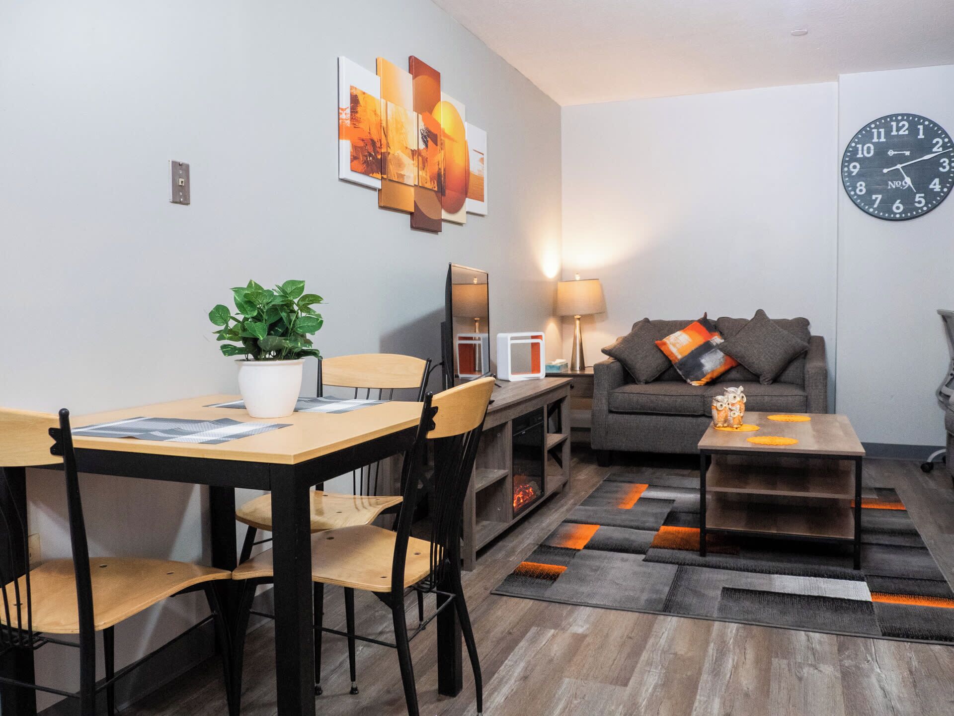 A modern living room with a dining area, a sofa, a coffee table, and a clock on the wall.