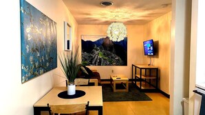A modern living room with a dining area, a large painting, a chandelier, and a flat-screen TV. - Stay Pittsburgh (Pittsburgh)