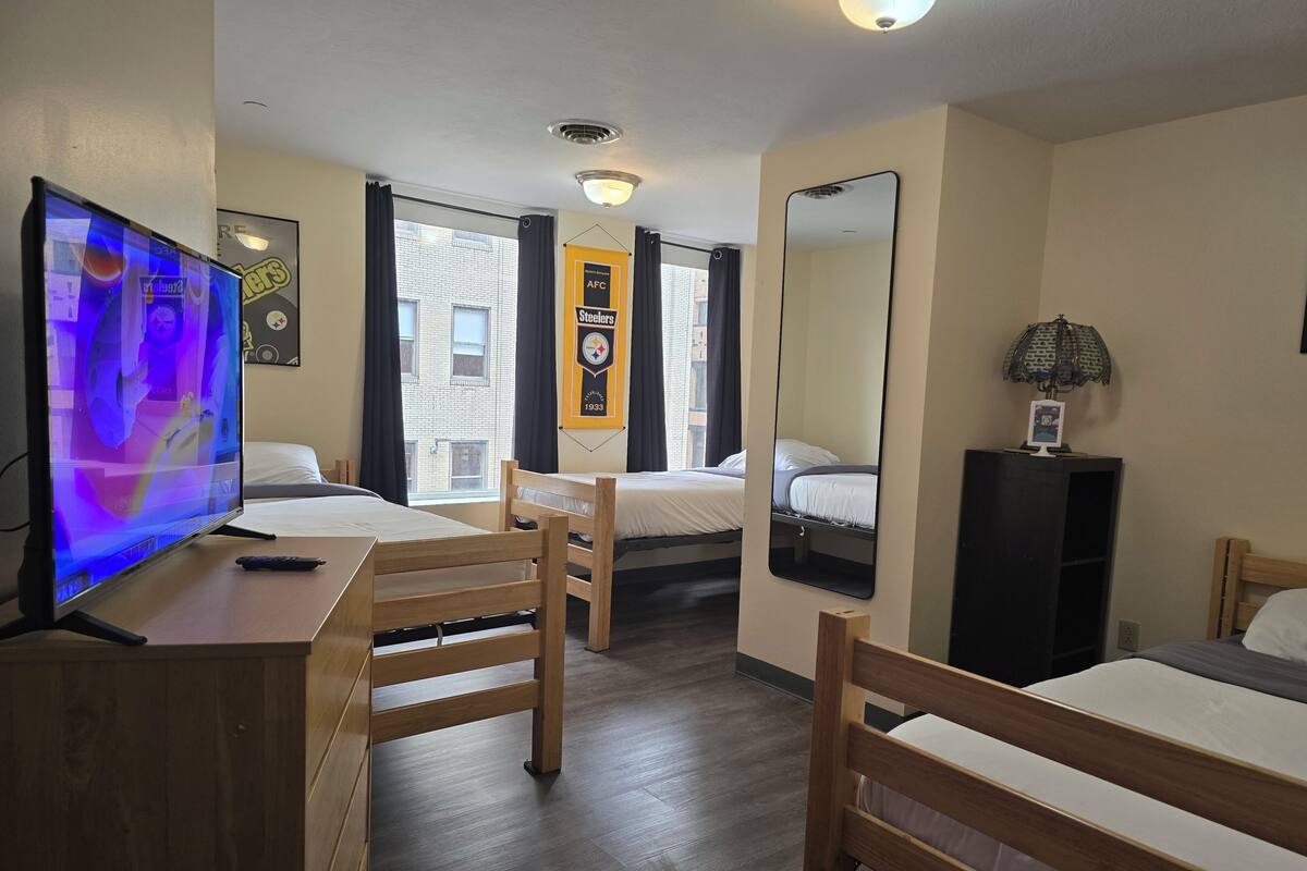 A hotel room with a TV, two beds, a desk, a mirror, and a window with curtains.