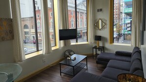 A modern living room with large windows, a flat-screen TV, a glass table, a sofa, and a lamp. - Stay Pittsburgh (Pittsburgh)