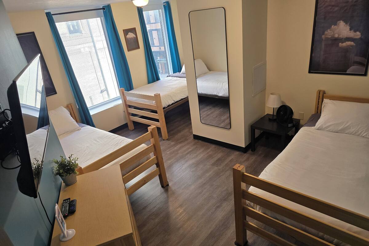 A hotel room with two beds, a desk, a chair, a TV, and a window with curtains.