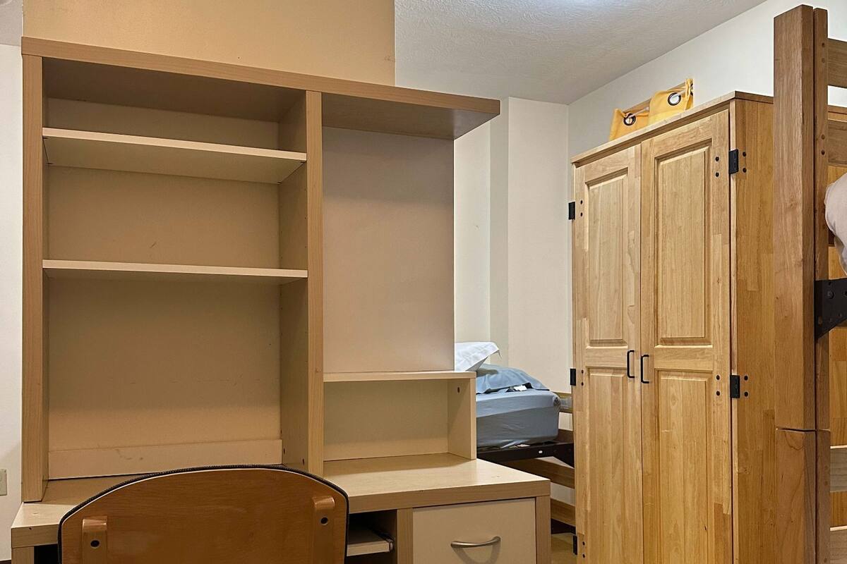 A bedroom with a wooden desk, a chair, a wardrobe, and a bed.