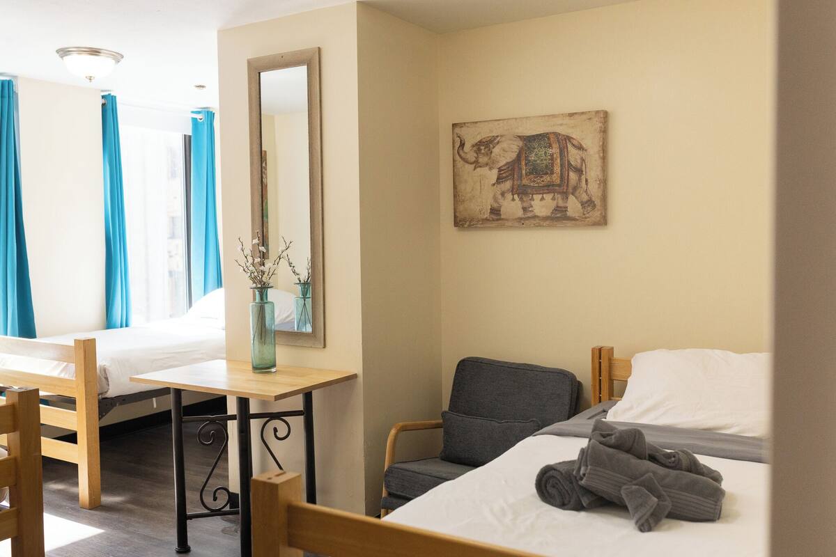 A hotel room with a bed, a desk, a chair, a mirror, and a wall-mounted elephant painting.