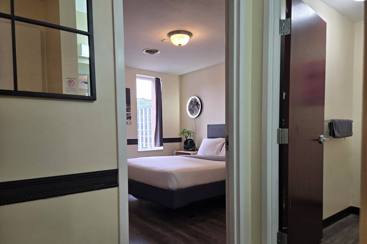 A hotel room with a bed, bedside table, lamp, and a window with curtains.