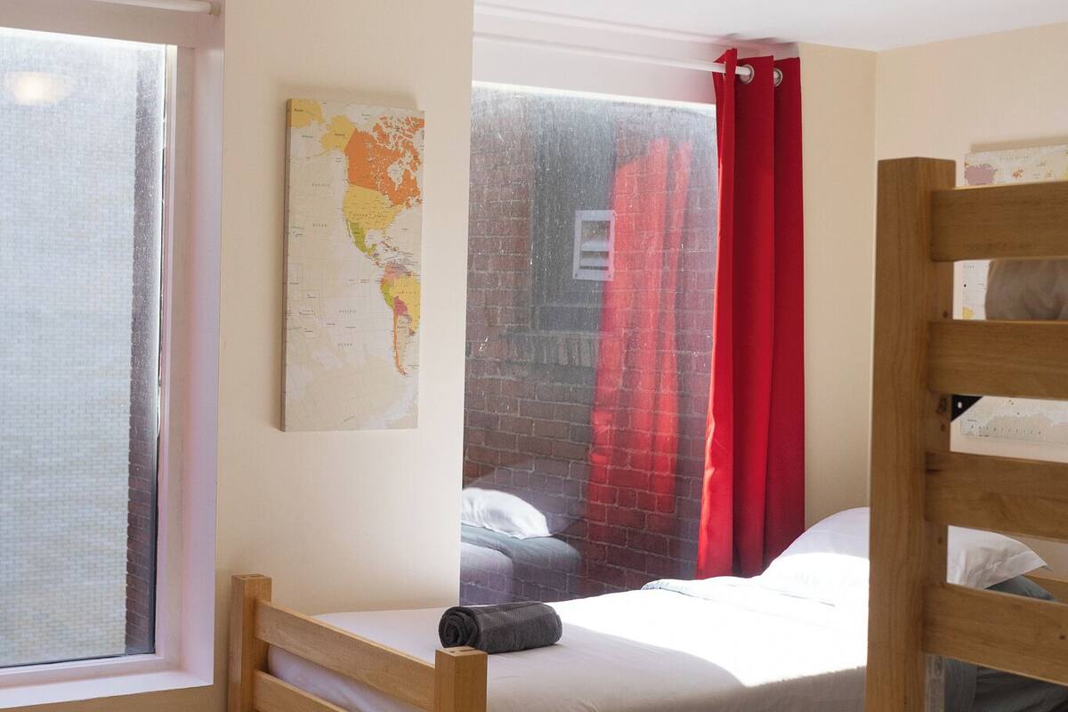 A room with a bunk bed, a window with a view, a map on the wall, and a red curtain.