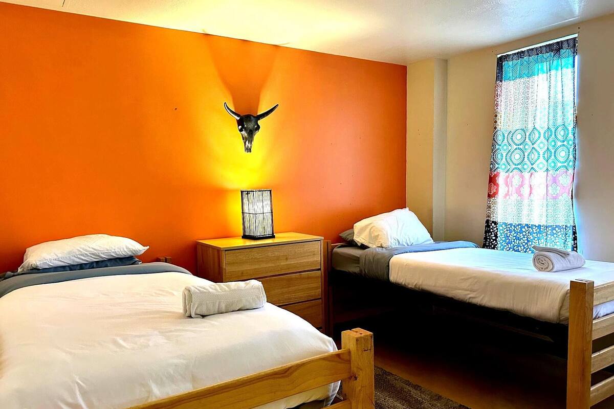 A room with two single beds, a wooden nightstand with a lamp, and a wall-mounted skull decoration.