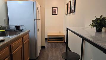 A kitchen with a refrigerator, sink, wooden cabinets, a small stool, and a potted plant.