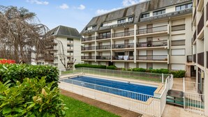 A multi-story residential building with balconies, a swimming pool, and a well-maintained garden area. - Studio Conac - Welkeys (Trouville-sur-Mer)