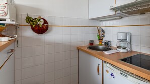 A kitchen with white cabinets, a sink, a coffee maker, and a clock on the wall. - Studio Conac - Welkeys (Trouville-sur-Mer)