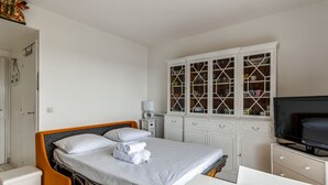 A hotel room with a bed, a TV, a white cabinet with glass doors, and a small table. - Studio Conac - Welkeys (Trouville-sur-Mer)