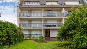 A multi-story residential building with balconies, a front door, and a small garden area with grass and plants. - Studio Conac - Welkeys (Trouville-sur-Mer)
