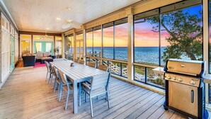 A wooden deck with a table and chairs, a grill, and large windows overlooking the sea. - Flamingo Bay - Bay Front, St George Plantation, Pet Friendly! (st. George Island)