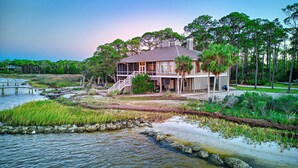 A house with a porch, surrounded by water and greenery. - Flamingo Bay - Bay Front, St George Plantation, Pet Friendly! (st. George Island)