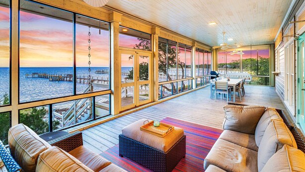 A spacious deck with a view of the ocean and pier, furnished with sofas and a dining area. - Flamingo Bay - Bay Front, St George Plantation, Pet Friendly! (st. George Island)