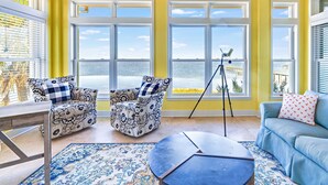 A room with large windows, a blue sofa, a patterned armchair, and a small table. - Flamingo Bay - Bay Front, St George Plantation, Pet Friendly! (st. George Island)