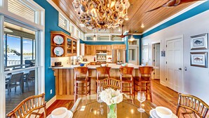 A spacious kitchen with wooden cabinets, a central island, and a dining area with a glass table and chairs. - Flamingo Bay - Bay Front, St George Plantation, Pet Friendly! (st. George Island)