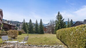 A wooden deck with two white chairs, a well-maintained lawn, and a hedge. - Appartement Lanura - Welkeys (Megève)