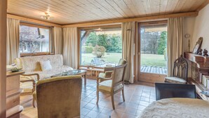 A cozy room with a wooden ceiling, a sofa, a dining table with chairs, and large windows offering a view of the outdoors. - Appartement Lanura - Welkeys (Megève)