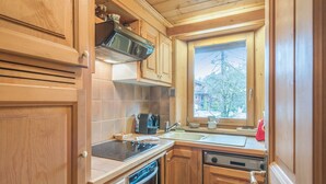 A compact kitchen with wooden cabinets, a built-in oven, a stovetop, and a window providing a view of the outdoors. - Appartement Lanura - Welkeys (Megève)