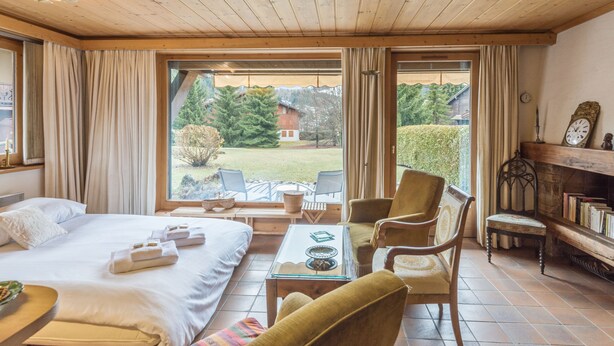 A hotel room with a bed, two chairs, a small table, a fireplace, and a view of the outdoors. - Appartement Lanura - Welkeys (Megève)