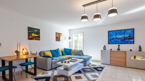 A modern living room with a grey sofa, blue and yellow cushions, a white coffee table, and a patterned rug. - Appartement du Brost - Résidence le clôt des Sarments - Welkeys (La Croix-Valmer)