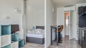 A modern hotel room with a bed, a desk, a television, and a kitchenette. - Appartement Rivage - Welkeys (Cagnes-sur-Mer)