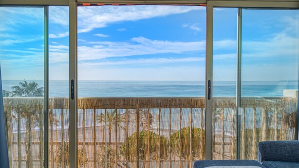 A room with a large sliding glass door leading to a balcony with a view of the ocean. - Appartement Rivage - Welkeys (Cagnes-sur-Mer)