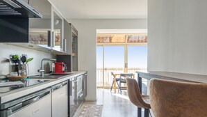A modern kitchen with stainless steel appliances, a red coffee maker, and a view of a balcony with a wooden fence. - Appartement Rivage - Welkeys (Cagnes-sur-Mer)