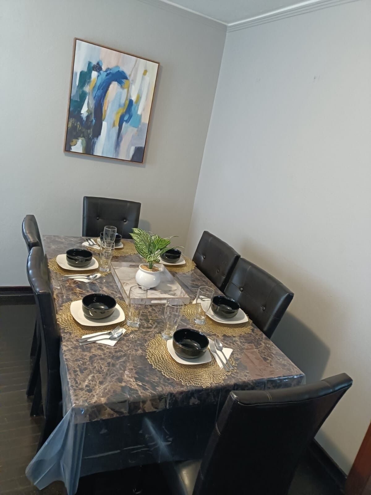 A dining area with a marble table, black chairs, and a painting on the wall.