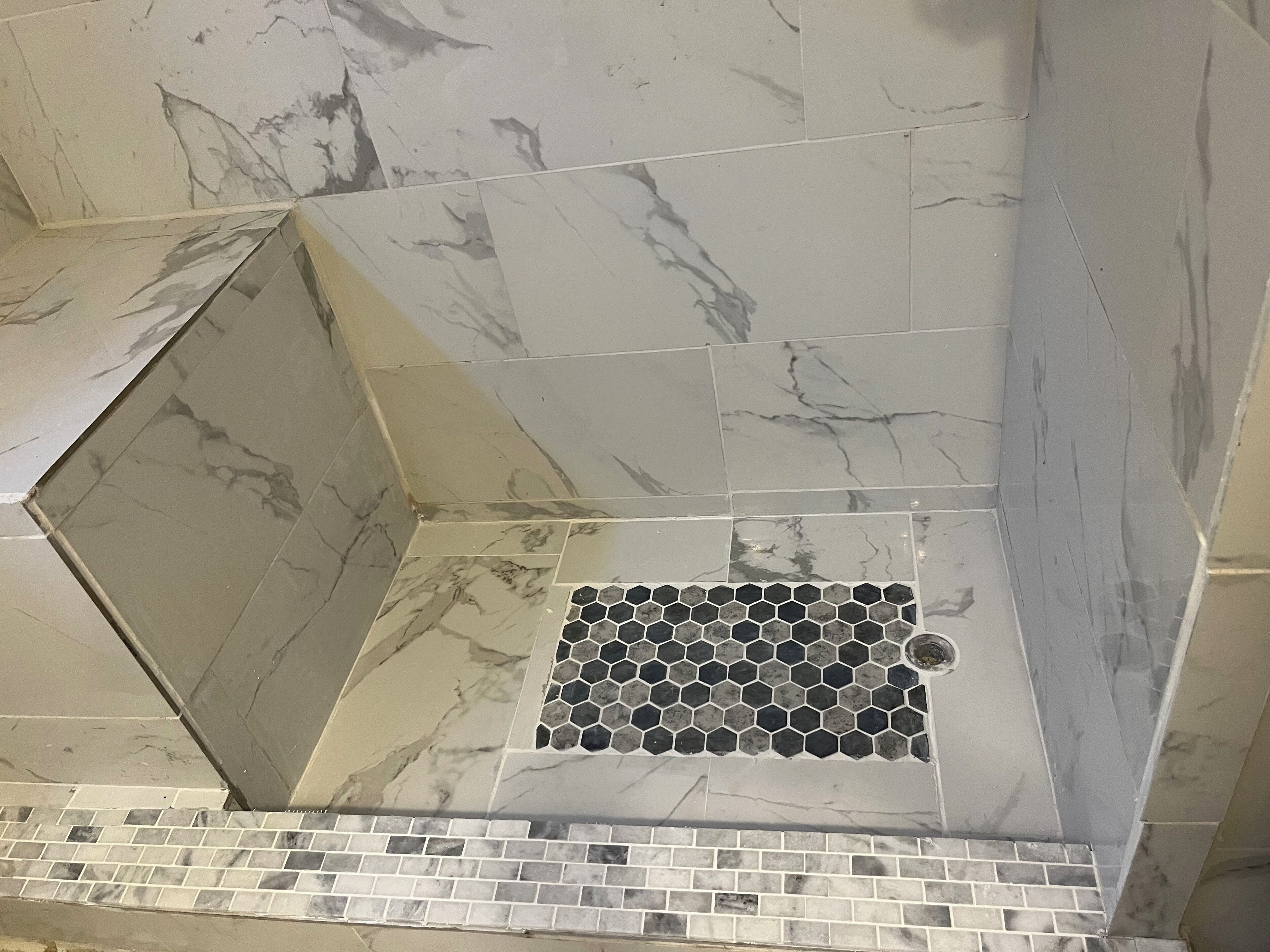 A bathroom with marble tiles and a hexagonal tile pattern near the floor.